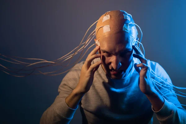 Un joven con la cabeza enredada en cables, experimentando dolor y sufrimiento —  Fotos de Stock