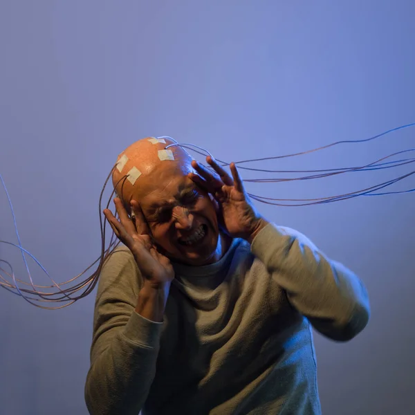 A young man with his head entangled in wires, screaming clutching his head, — Stock Photo, Image