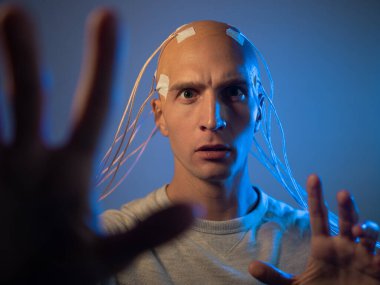 Kafası kabloya dolanmış genç bir adam ellerini öne çekiyor.,