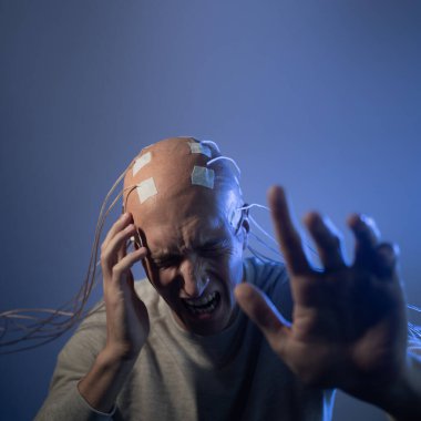 Kafası tellere dolanmış, başını tutarak bağıran genç bir adam.,