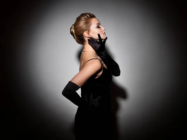 A femme fatale in a black dress with an open back and long velvet gloves. — Stock Photo, Image