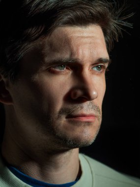 Düşünceli üzgün bir adam sağa bakar. Yan ışıkta portre,