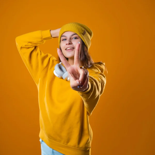 Elegante joven morena alegre con capucha amarilla muestra un gesto de victoria — Foto de Stock