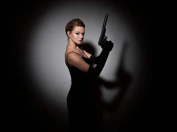 Espía peligroso. Una mujer fatal en un vestido negro con la espalda abierta sostiene una pistola — Foto de Stock