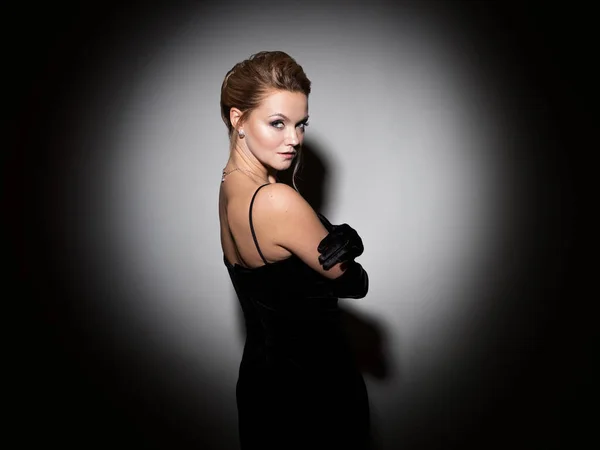 A femme fatale in a black dress with an open back and long velvet gloves. — Stockfoto