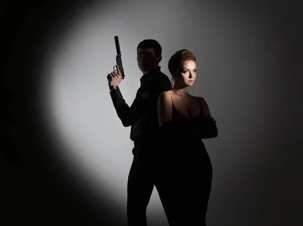 Σούπερ πράκτορες, μια πανέμορφη ξανθιά με μαύρο βραδινό ντύσιμο και ένας άντρας με όπλο. — Φωτογραφία Αρχείου