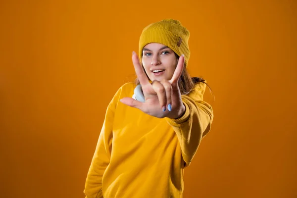 Élégant jeune brune joyeuse dans un sweat à capuche jaune et chapeaux montre geste cool, — Photo