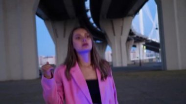 Pembe ceketli, açık havada neon ışıklarla dans eden tatlı, genç bir esmer.,