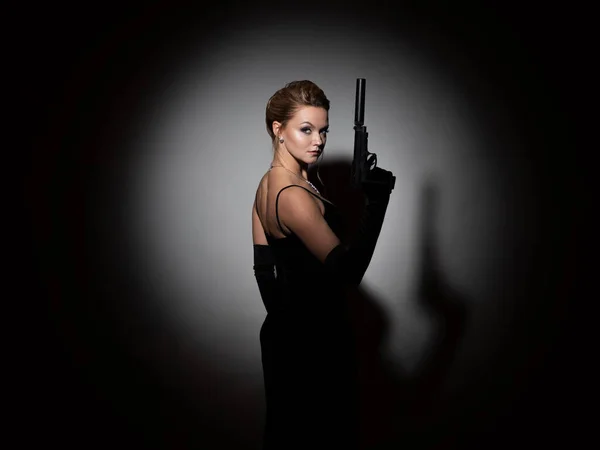 Gefährlicher Spion. Eine Femme fatale im schwarzen Kleid mit offenem Rücken hält eine Pistole in der Hand — Stockfoto