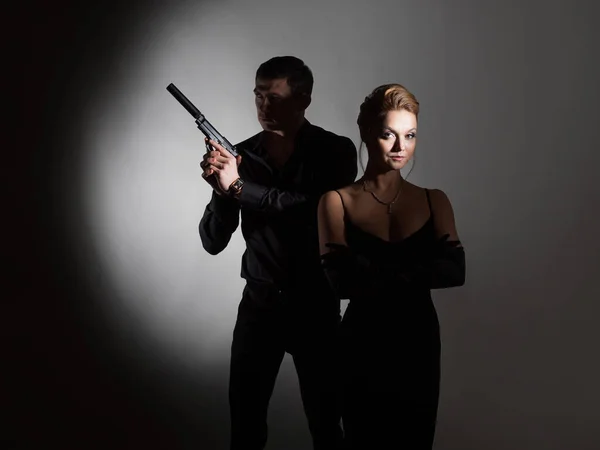 Σούπερ πράκτορες, μια πανέμορφη ξανθιά με μαύρο βραδινό ντύσιμο και ένας άντρας με όπλο. — Φωτογραφία Αρχείου