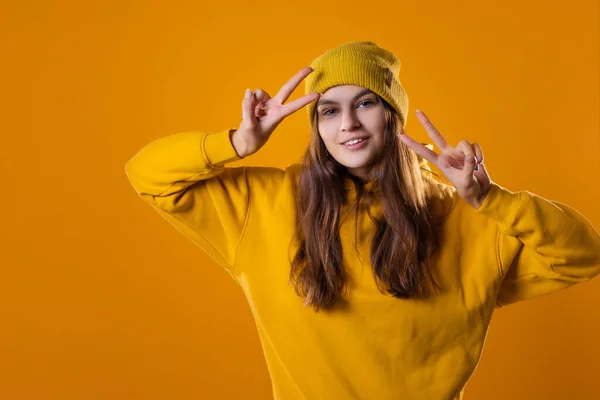 Elegante alegre jovem morena em um capuz amarelo mostra um gesto de vitória — Fotografia de Stock