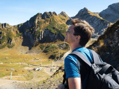 Sırt çantalı genç bir adam dağ manzarasının tadını çıkarıyor.,