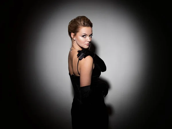 A femme fatale in a black dress with an open back and long velvet gloves. — Stockfoto