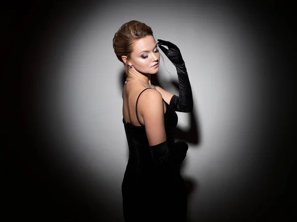 A femme fatale in a black dress with an open back and long velvet gloves. — Stockfoto