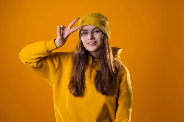 Стильна весела молода брюнетка в жовтому светрі показує жест перемоги — стокове фото