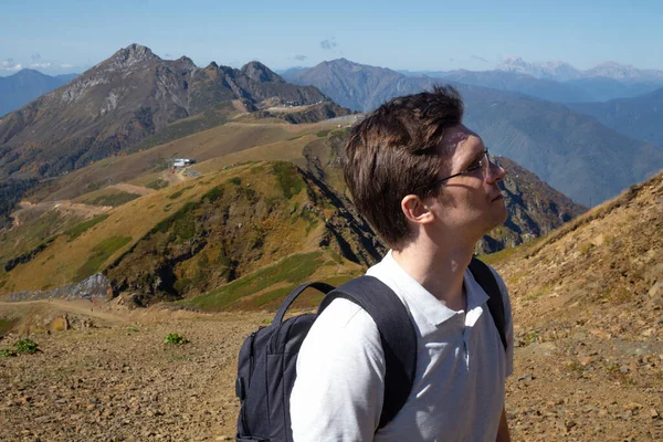 Un giovane con uno zaino si guarda intorno godendo il paesaggio di montagna, — Foto Stock