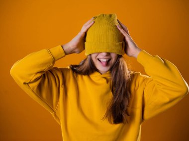 Sarı kapüşonlu genç bir kadın ve sarı arka planda bir şapka..