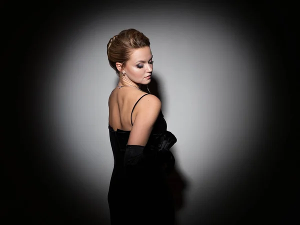 A femme fatale in a black dress with an open back and long velvet gloves. — Stockfoto