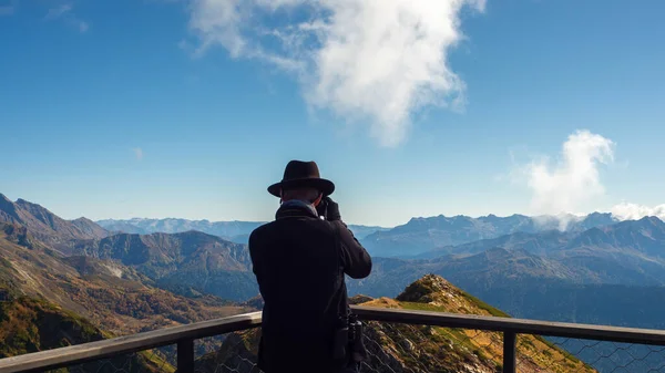 En fotograf i bergen, en resenär i hatt tar ett foto Stockbild