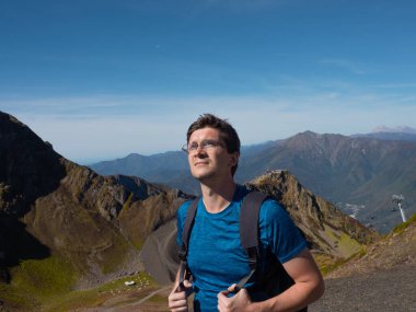 Sırt çantalı genç bir adam dağ manzarasının tadını çıkarıyor.,