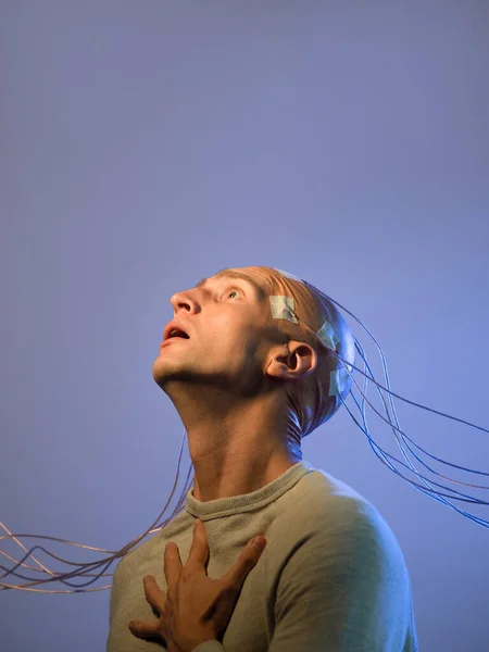 Un joven con la cabeza enredada en cables, experimentando dolor y sufrimiento —  Fotos de Stock