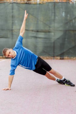 Gri eşofmanlı yakışıklı bir adamın portresi. Bir elinde şınav çekiyor. 
