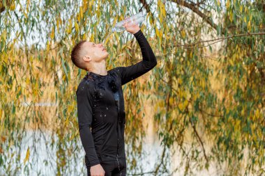 Genç bir adam, antrenmandan sonra atlet yüzüne şişeden su döker.