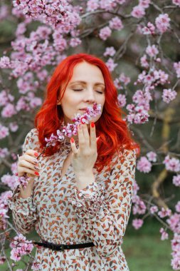 Kırmızı pembe çiçekli, çiçek açan bir ağacın arka planında güzel, mutlu, genç bir kadın. Bahar ve güzellik