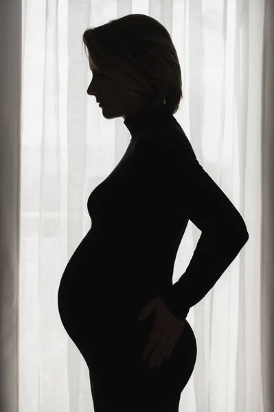 Pregnant woman against window — Stockfoto