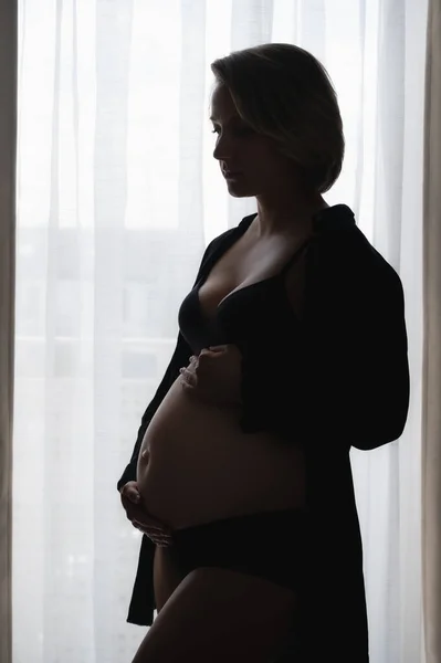 Donna incinta contro la finestra Foto Stock Royalty Free