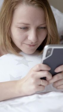 Yatakta cep telefonu kullanan kadın.