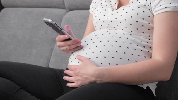 自宅でソファに座っている間 妊娠中の女性が携帯電話にSmsメッセージを入力します スマートフォンで認識されていない妊婦のテキスト — ストック動画
