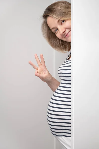 Gravid Kvinna Kikar Genom Vit Vägg Och Visar Tre Fingrar — Stockfoto