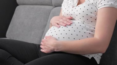 Hamile kadın evdeki koltukta otururken cep telefonu kullanıyor. Akıllı telefonu olan tanınmamış hamile bir kadın..