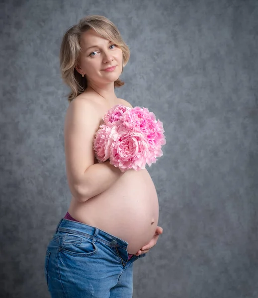 裸体で花を持つ美しい妊婦 露出した妊娠中の腹を持つ女性カメラを見て — ストック写真