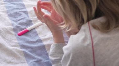 Mutlu kadın yatakta yatıyor ve hamilelik testi yapıyor. Tanımlanamayan bir kız iki çizgili pozitif hamilelik testi tutuyor. Hamilelik konsepti, aile planlaması.