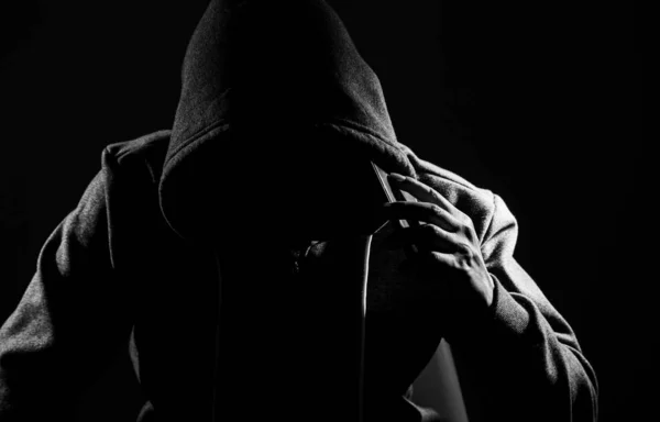 Scammer Using Smartphone to make a call. Men in black clothes with hidden face.