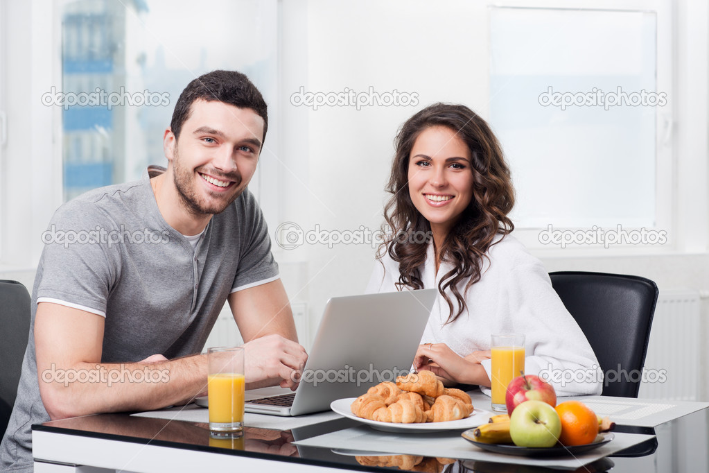 Beautiful couple having breakfast with a laptop