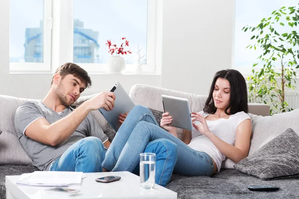 Couple sitting on a couch with tablet computers — Stock Photo, Image