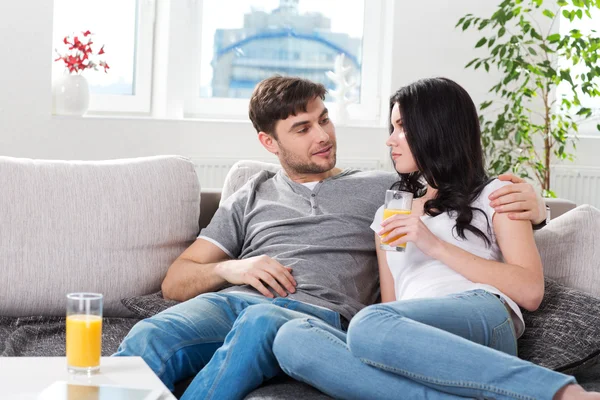 Paret sitter på soffan och dricka apelsinjuice — Stockfoto