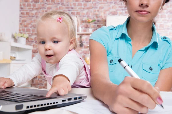 Kvinna med baby i köket arbetar med laptop — Stockfoto