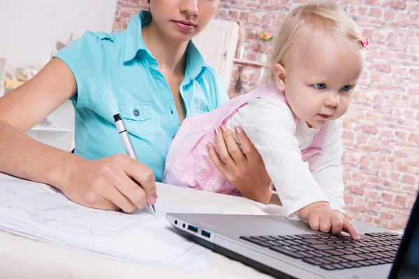 ノート パソコンを扱う台所で赤ちゃんを持つ女性 — ストック写真