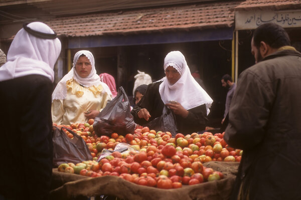Завуалированные арабские женщины покупают яблоки на уличном рынке
