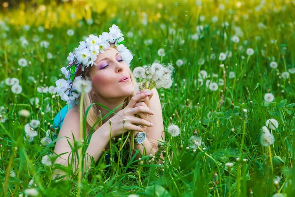 Giovane donna che soffia un dente di leone sui campi — Foto Stock