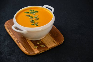 Kabak tohumlu balkabağı kremalı çorba. Beyaz kasede fesleğenle servis edilen siyah desenli arka plan, üst manzara, kopyalama alanı.