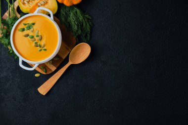 Kabak tohumlu balkabağı kremalı çorba siyah desenli arka planda fesleğenle servis edilir, üst manzara, kopyalama alanı