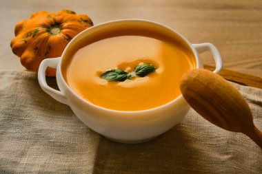 Fesleğenli ev yapımı balkabağı çorbası. Kırsal bir masada tahta bir kaşık. Mevsimlik güz yemeklerinin en iyi manzarası, sağlıklı ve taze..