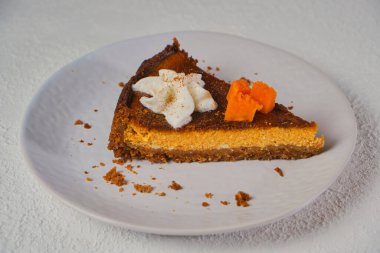 Ev yapımı balkabaklı peynirli kek. Gri tabakta krem şanti ile süslenmiş. seçici odak, beyaz desenli arkaplan