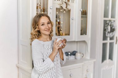 Şenlikli Noel atmosferi konsepti, dekore edilmiş oturma odasında çay içen genç ve güzel bir kadın.