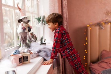 Ekose pijamalı sevimli çocuk, pencereden bakıyor, sabırsızlıkla Noel Baba 'yı bekliyor ve hediyeler alıyor.